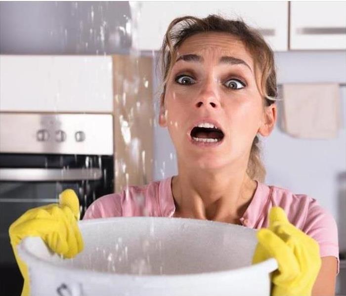 Woman holding a bowl to catch water from a ceiling leak.